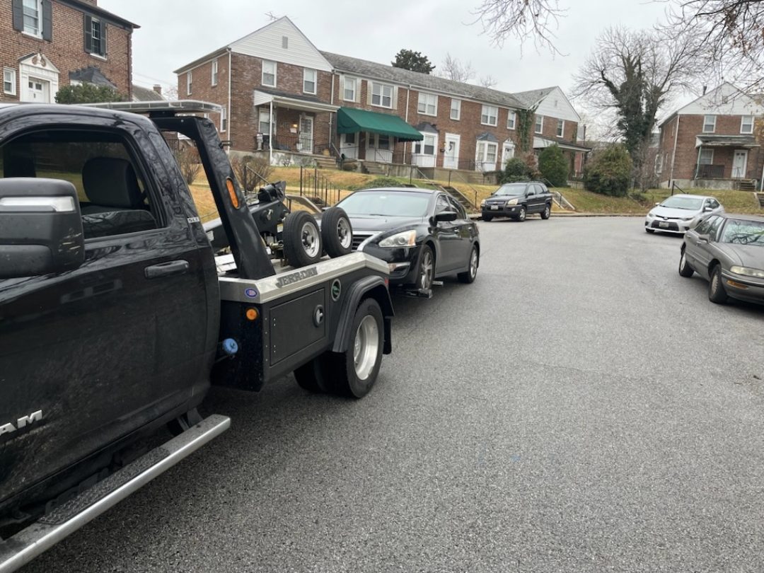 Wheel-lift tow truck hooking a sedan on a Baltimore rowhouse street